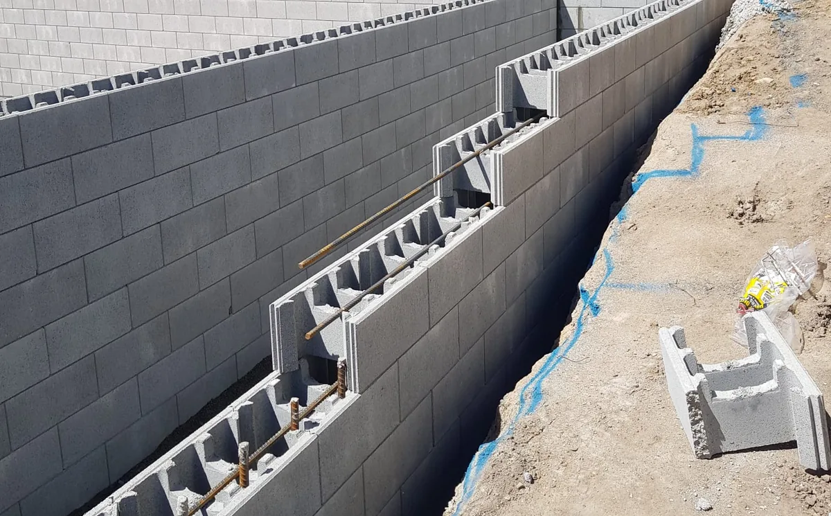 Grey concrete blockwork retaining wall with vertical steel starter bars ready for core filling
